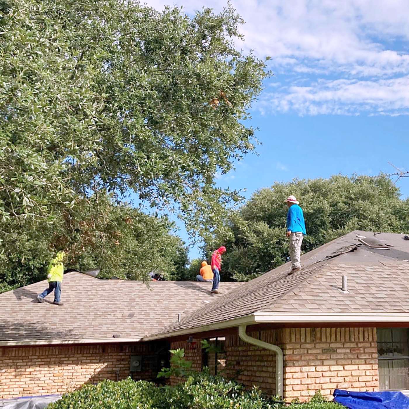 A crew stripping the old shingles off a single-story brick home