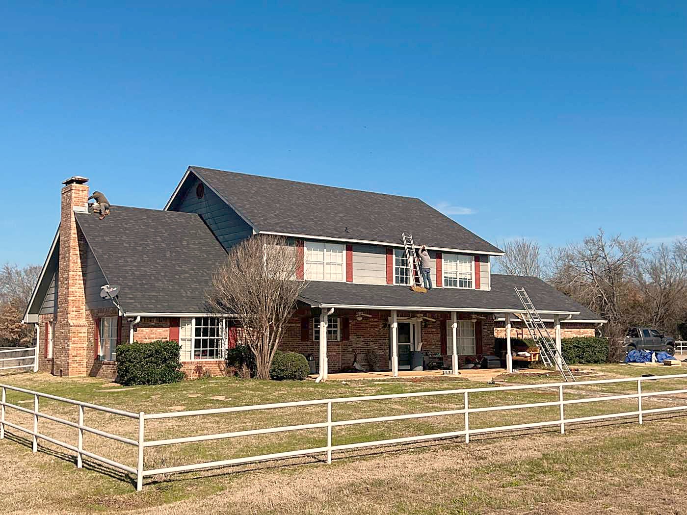 A two-story home behind a white rail fence with a newly finished roof