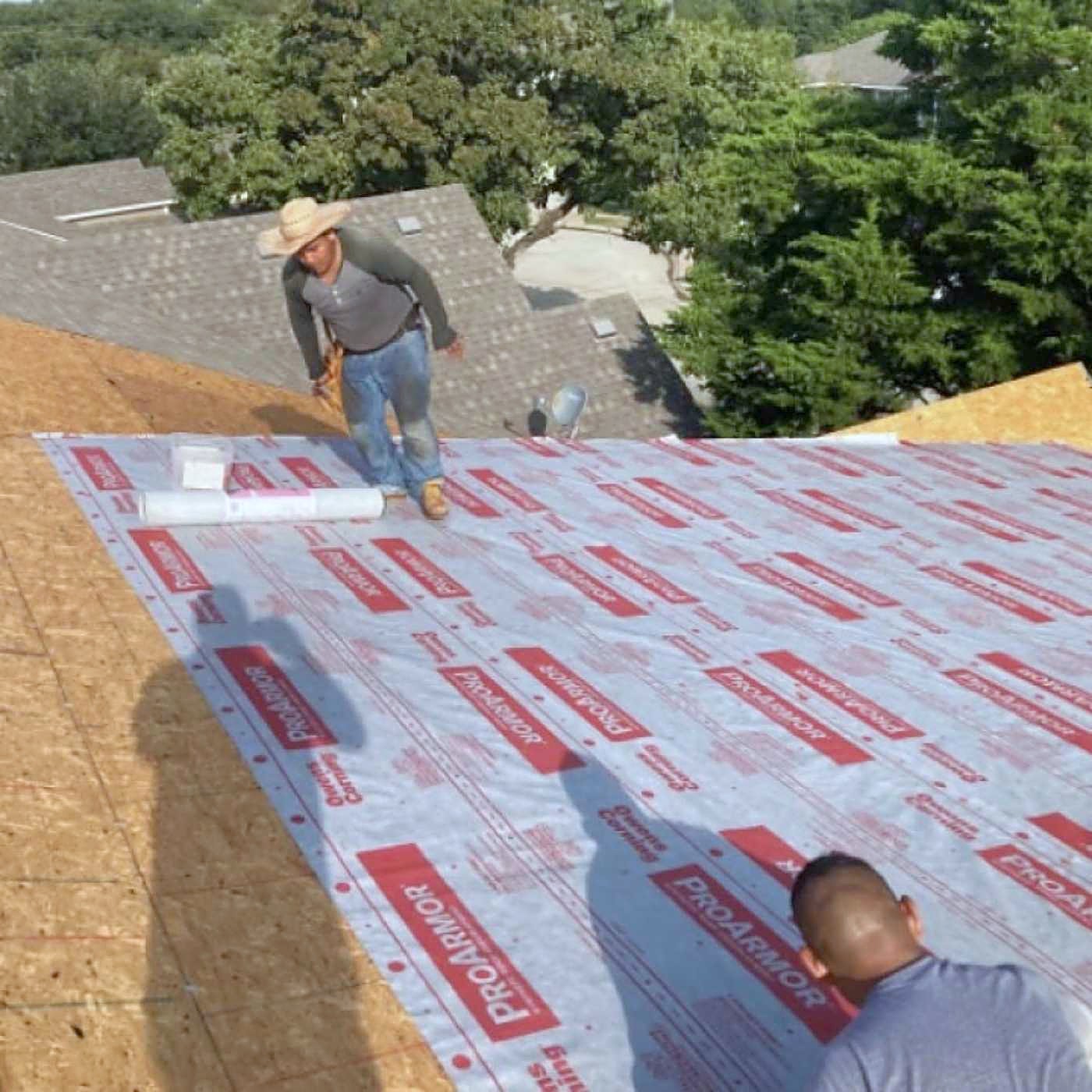 A roofer rolling synthetic underlayment across bare decking
